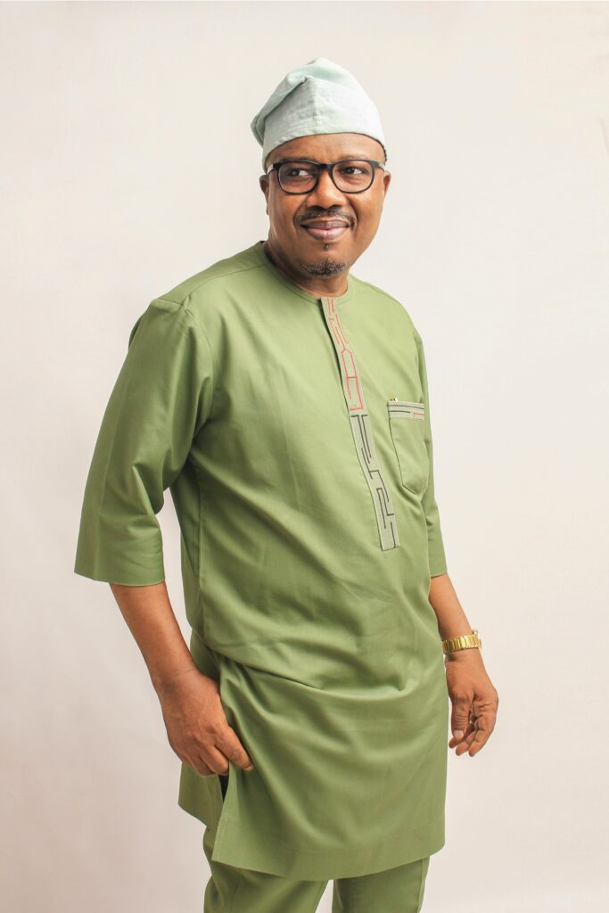 Portrait of a stylish man wearing traditional green attire, smiling in a studio shot.